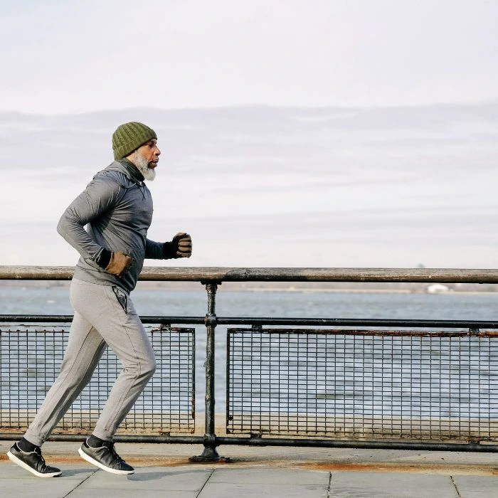 hombre senior corriendo abrigado junto al mar - Imottus